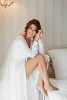 Fashion shot, beautiful woman in a dressing gown. Fashion, glamor concept. The morning of the bride, the bride in a dressing gown sits by the bed and looks at the camera photo