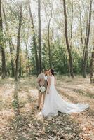 Wedding photo. The bride and groom stand tenderly kissing in the forest. Long train of a wedding dress. Couple in love. Summer light. The shadows photo