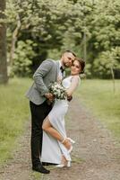 the bride in a white evening dress poses with the groom with a beautiful hairstyle, the groom gently wraps the bride and leans against her. Portrait photo