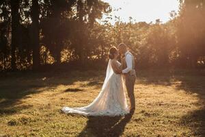 Wedding photo. The bride and groom are standing in a beautiful forest and beautiful light, hugging and leaning their noses against each other. Couple in love. Stylish groom photo