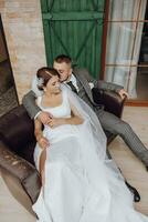 the bride and groom are sitting on a sofa against the background of green windows. Stylish bride and groom. Wedding photo. easy atmosphere photo