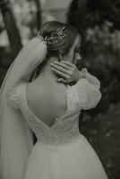 Hairstyle with an elegant wedding hair accessory. Photo from the back. Gently touches the veil. Beautiful and light dress. Black and white photo