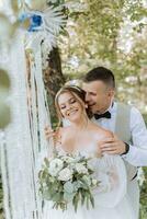 Groom and bride on the wedding day, walking outdoors. The groom hugs the bride from behind by the shoulders. People are happy and smile. Happy couple in love looking at each other photo