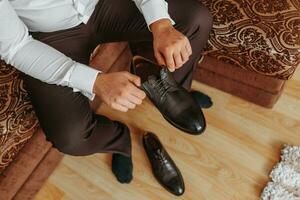 groom tied the laces on the shoes close up. business man is hanging shoes indoor in hotel room. mans hands and pair of leather men's shoes. meeting of the bridegroom. business man's morning. photo