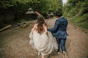 A happy wedding couple is running along a forest path. Groom and bride. Wedding photo session in nature. Photo session in the forest of the bride and groom.