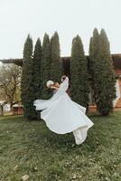 Handsome groom carrying a beautiful laughing bride in his arms in a spring park. The groom is circling with the bride in his arms photo