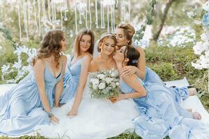 The bridesmaids are in blue dresses, the bride is holding a beautiful bouquet. Sitting enjoying the celebration. Beautiful luxury wedding blog concept. Spring wedding. photo