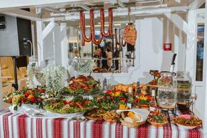 Buffet table at the wedding. An assortment of snacks on white plates standing on a Ukrainian-style tablecloth. Banquet service. Food, snacks with cheese, ham, prosciutto and greens. photo