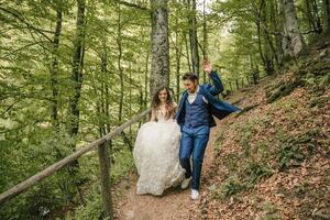 A happy wedding couple is running along a forest path. Groom and bride. Wedding photo session in nature. Photo session in the forest of the bride and groom.