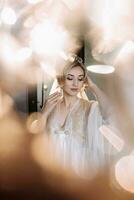 Blonde bride poses in a robe and tiara, wedding portrait. Reflections and reflections of glass. wedding photo in a light key