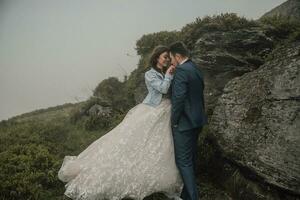 Happy wedding couple in the mountains near a big stone. The groom kisses the bride's hand. Wedding photo session in nature. Photo session in the forest of the bride and groom.