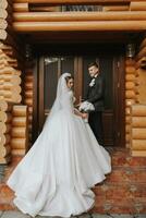 Handsome groom and charming bride stay together near modern wooden house in park photo
