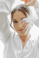 Mañana de novia antes de el boda. hermosa joven mujer con largo velo en un blanco túnica. natural belleza y profesional maquillaje.chica en blanco cordón tocador vestido. foto