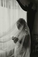 A brunette bride in a white dress holds her silver wedding ring. French manicure. Open shoulders. Beautiful hands. Long veil. Morning of the bride. Details. black and white photo