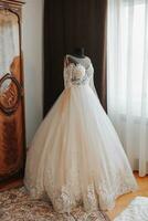 An exquisite wedding dress with lace sleeves on a black mannequin in the bride's room. High quality photo. Wedding details. White voluminous dress with embroidery photo