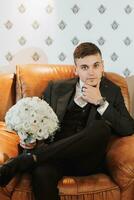 novio con un ramo de flores de flores en un habitación con un maravilloso interior. el novio es mirando a el cámara foto