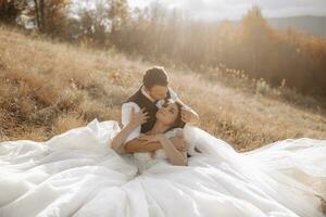 portrait of a stylish groom with a bride on a background of autumn dry grass. the concept of a rural wedding in the mountains, happy bohemian newlyweds. the bride and groom are lying on the grass photo