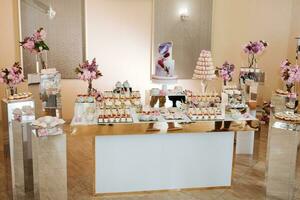 delicioso Boda recepción caramelo bar postre mesa lleno con pasteles y dulces y flores chino Cereza flores en el antecedentes de un Exquisito restaurante foto