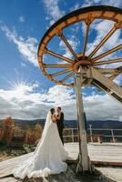 Married couple among mountains, bride looking at groom, hugging, girl smiling, woman in white wedding dress, groom and brown suit photo