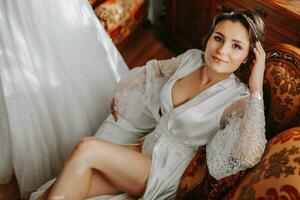 beautiful bride on a retro sofa in a robe with open legs, full length photo. Wedding hairstyle, light makeup photo
