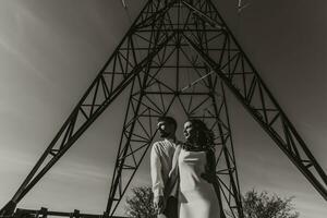 elegante modelo Pareja en el montañas en verano. un joven chico y niña en un blanco seda vestir son en pie cerca grande estructuras de poder líneas. negro y blanco contraste foto