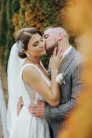 el novia y novio acurrucado arriba a cada otro tiernamente un Pareja de recién casados, novia y acicalar, a un Boda en el naturaleza de verde arboles foto retrato Boda Pareja