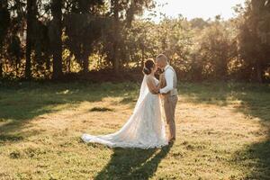 Wedding photo. The bride and groom are standing in a beautiful forest and beautiful light, hugging and leaning their noses against each other. Couple in love. Stylish groom photo
