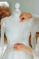 white wedding dress on a mannequin in the room, close-up of the bride's hand on the mannequin. Wedding details, modern wedding dress with long train, long sleeves and open back photo