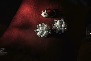 Silver bridal engagement ring with pearl and silver earrings with pearls on a red background. Beautiful light. Photo of wedding details.