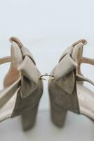 Photo of details at the wedding. An engagement ring with a diamond stands between gray shoes, velor sandals with decor on the foot, on the windowsill, on a white background. Contour line.