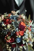 Beautiful wedding bouquet with different flowers in the hands. Rustic wedding bouquet with red and blue roses and white carnations. Close-up. Side view photo