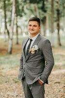 a stylish groom walks forward in the forest buttoning his jacket between tall trees. A fashionable groom, an adult man photo