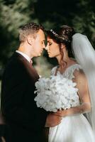 The groom and the bride are gently leaning on each other, holding a bouquet of white orchids photo