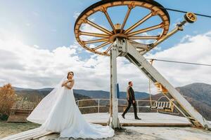 Married couple among mountains, bride looking back to groom, girl smiling, woman in white wedding dress, groom and brown suit photo