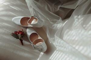 details of the bride on a soft pink chair, the wedding boutonniere and the bride's shoes are white photo