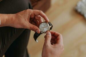 Close-up of a fashionable image of a luxury watch in hands. Detail of the body of a business man. Man's hand in brown pants pocket close-up on gray background. Clock close-up photo