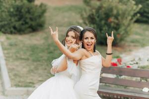 Boda foto en naturaleza. un morena novia en un blanco largo vestir y su amigo en un desnudo vestir son engañando alrededor juntos y sonriente atentamente. joven mujer. emociones