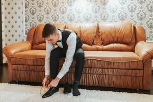 A stylish groom puts on shoes, prepares for the wedding ceremony. A large portrait. A wonderful interior in the morning light. Groom's morning photo