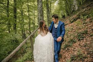 A happy wedding couple is running along a forest path. Groom and bride. Wedding photo session in nature. Photo session in the forest of the bride and groom.