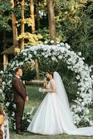 Beautiful wedding couple on the wedding autumn ceremony. the round arch is decorated with white flowers photo