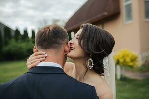 Portrait of the bride and groom in nature. Stylish bride and groom in a long lace dress are hugging and kissing near the trees in the garden. A happy couple in love photo