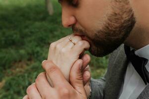 The groom kisses the fingers of the bride, tenderly holding her hand with a precious ring. Stylish groom photo