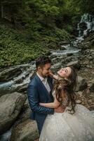 Portrait of a happy bride and groom near a waterfall. Bride and groom. Wedding photo session in nature. Photo session in the forest of the bride and groom.