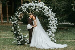 Happy bride and groom after wedding ceremony. round ceremonial arch. Long white dress of the bride photo
