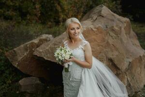 The bride is sitting on a rock high in the mountains next to a large stone. Wedding Dress. The wind tears the veil photo