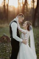 Boda foto. el novia y novio son caminando en el bosque. el novio abrazos el espalda de su amado. largo Boda vestido. un Pareja en amor entre alto arboles otoño luz de sol. foto