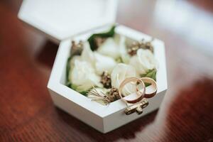 Photo of wedding accessories. Luxurious bouquet of the groom. Gold rings on a stand with flowers, white cufflinks on a wooden floor background.