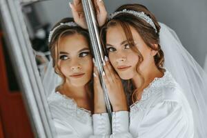 preparación para el boda. hermosa joven novia en un blanco Boda vestir en el habitación. lujo modelo mirando a cámara, reflexión en espejo. Mañana de el novia foto