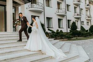 Groom and bride walking outdoors near a posh hotel. A long train of dress on the steps photo