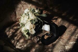 Accessories for the groom's wedding. A bouquet of white roses and greenery stands on the back of the sofa near the window. Beautiful flowers. Light and shadows photo